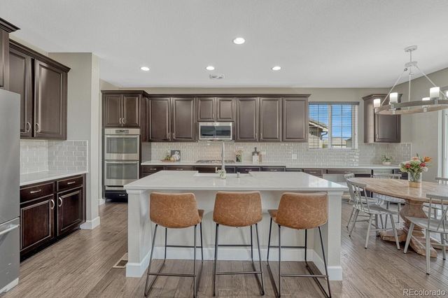 a kitchen with stainless steel appliances granite countertop a stove top oven a sink dishwasher a dining table and chairs with wooden floor