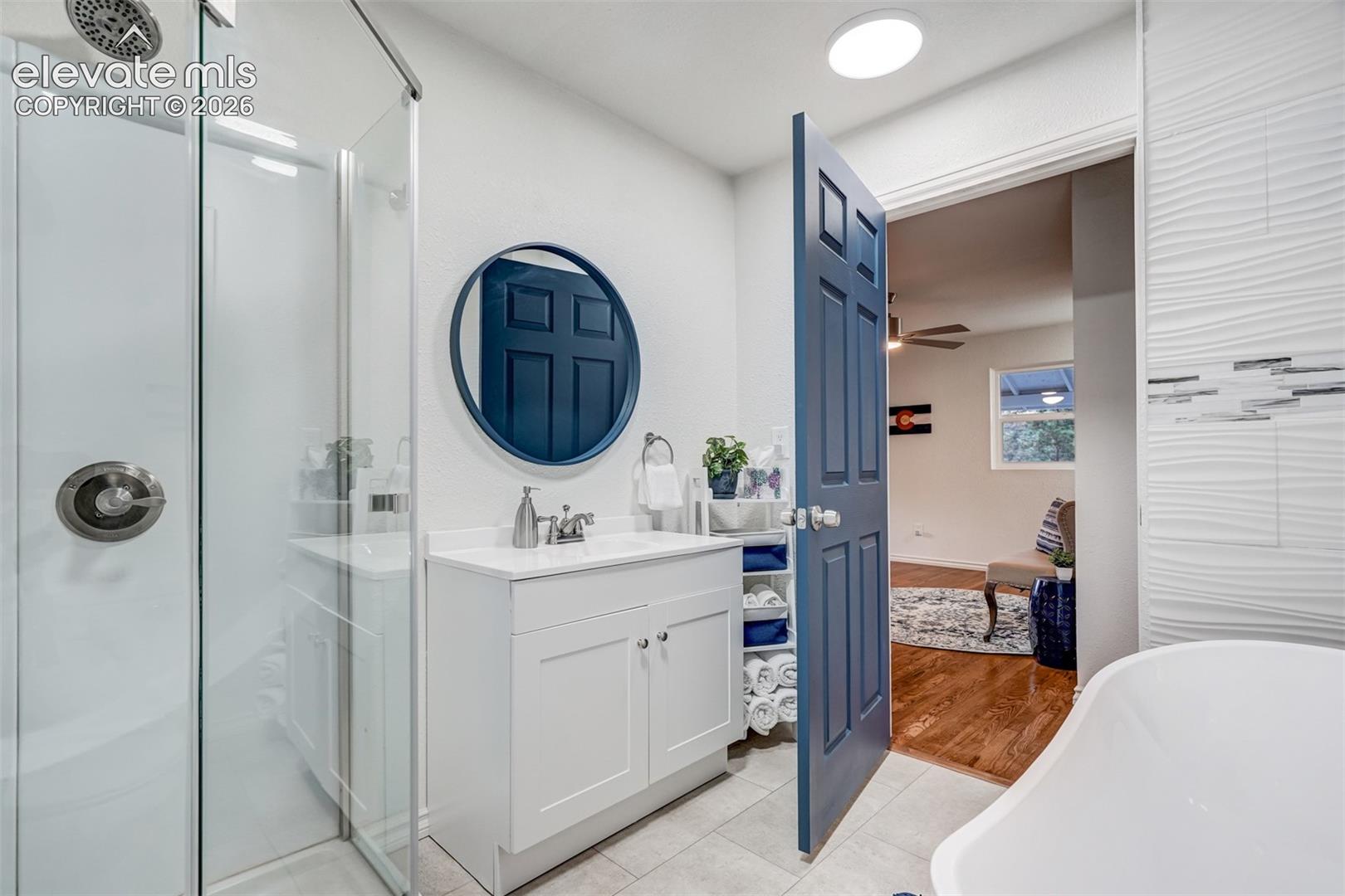 9955 Mesa Road Cascade, CO 80809 - Photo 22 of 41 Walk-in shower with glass enclosure, single vanity with white cabinetry, round wall mirror, and wave-patterned accent wall