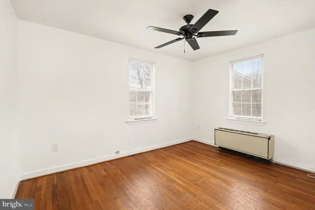 an empty room with wooden floor fan and windows