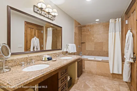 a bathroom with a granite countertop double vanity sink a mirror and a shower