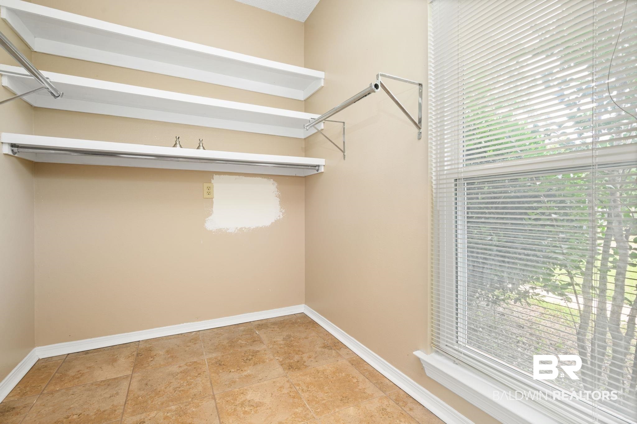 7540 2 Mile Road Irvington, AL 36544 - Photo 28 of 82 Interior space featuring multi-tier shelving, integrated hanging rods, a large window with blinds, and tile flooring