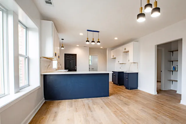 a large kitchen with stainless steel appliances kitchen island granite countertop a refrigerator a sink dishwasher a stove and a dining table with wooden floor