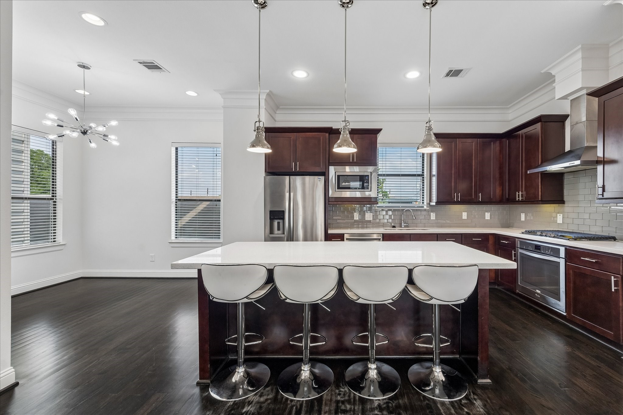 734 West 20th Street, Unit A Houston, TX 77008 - Photo 2 of 23 Chef’s kitchen features a large island w/ breakfast bar seating, stainless appliances, gas range, glass subway tile backsplash, soft-close cabinetry & crown molding. Adjacent dining area includes a bar with wine chiller—ideal for entertaining.