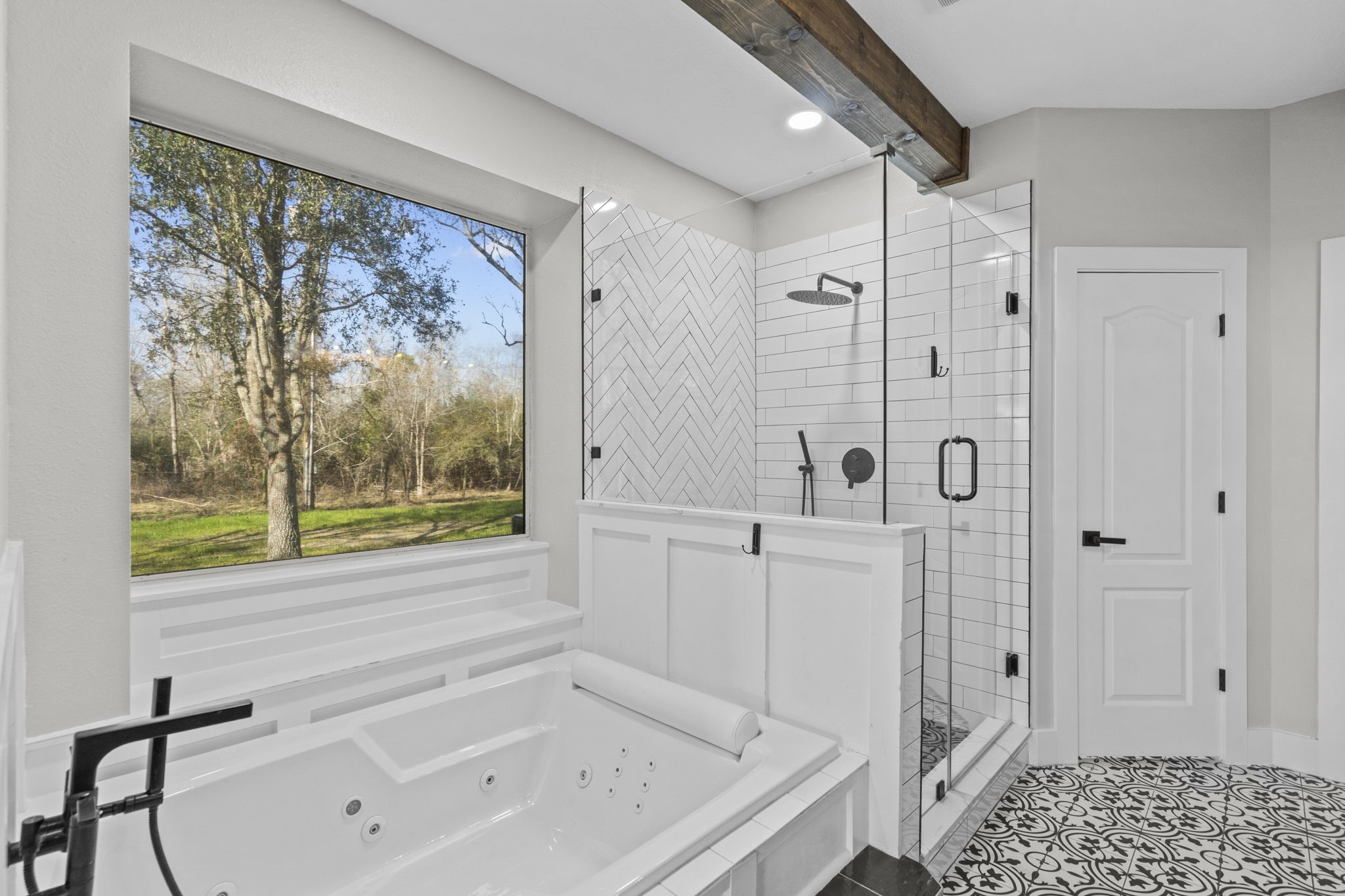 2730 Lawrence Road Kemah, TX 77565 - Photo 25 of 46 This bathroom features a large soaking tub with a view of the outdoors, a modern glass-enclosed shower with sleek black fixtures, and elegant patterned tile flooring. The design is bright and contemporary, offering a spa-like ambiance.