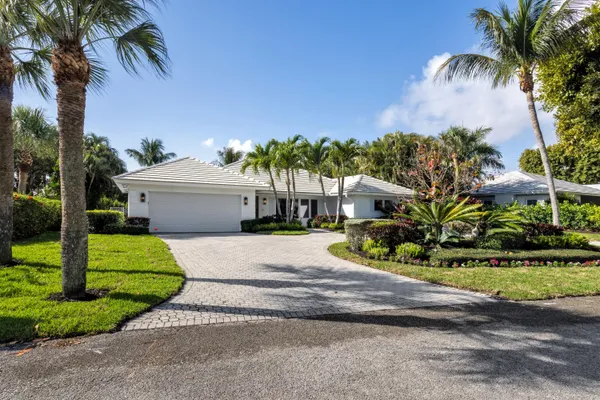 a white house with a yard and table and chairs under palm trees