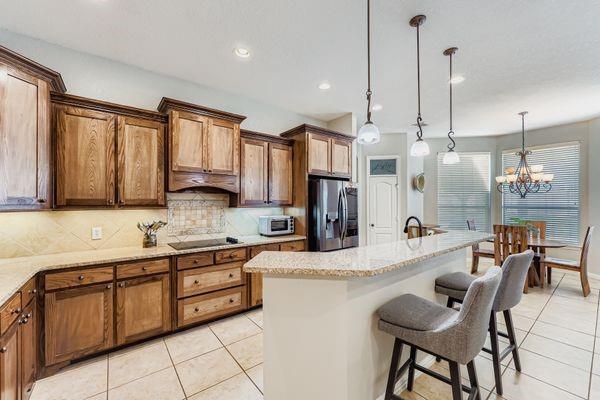 602 Christa Street Ovilla, TX 75154 - Photo 11 of 23 Kitchen with brown cabinetry, light tile patterned floors, a breakfast bar area, decorative light fixtures, and tasteful backsplash