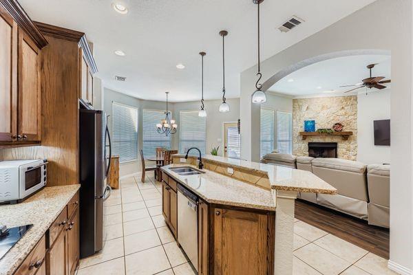 602 Christa Street Ovilla, TX 75154 - Photo 12 of 23 Kitchen with brown cabinetry, light stone counters, a fireplace, pendant lighting, and light tile patterned floors