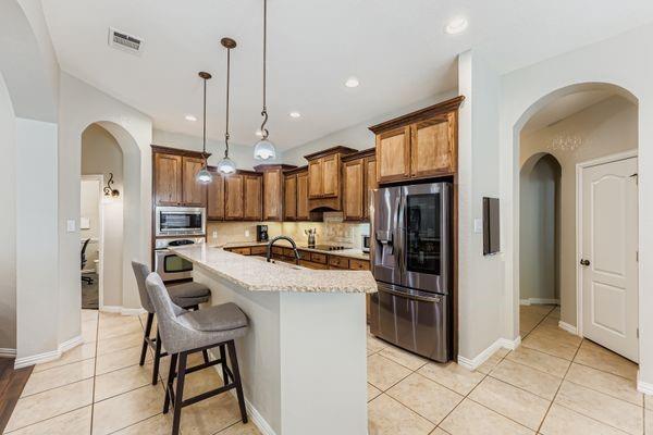 602 Christa Street Ovilla, TX 75154 - Photo 8 of 23 Kitchen with arched walkways, decorative backsplash, light tile patterned floors, appliances with stainless steel finishes, and a kitchen bar