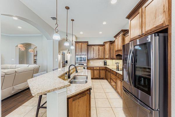602 Christa Street Ovilla, TX 75154 - Photo 10 of 23 Kitchen with stainless steel appliances, a breakfast bar area, light tile patterned floors, pendant lighting, and light stone counters