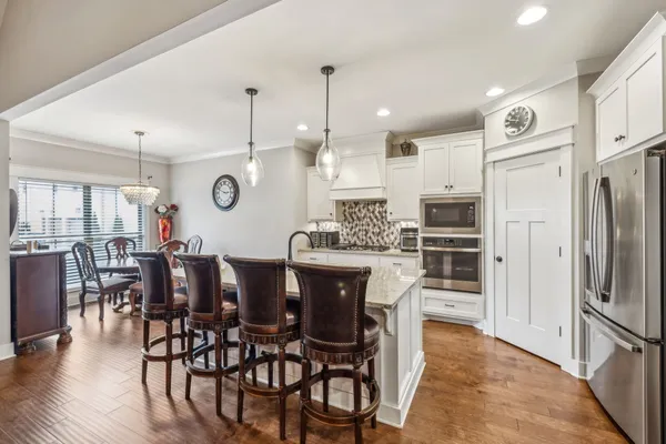 a kitchen with stainless steel appliances kitchen island granite countertop a dining table chairs and white cabinets