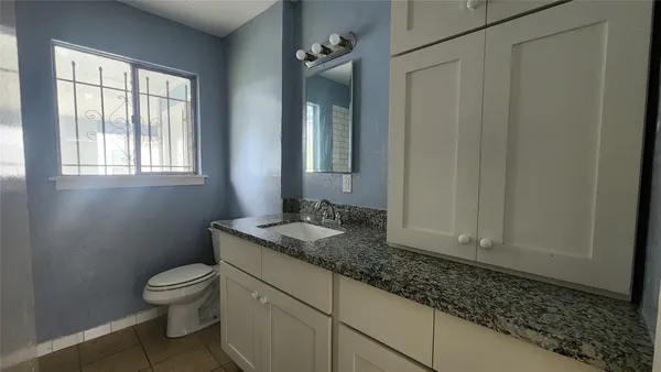 a bathroom with a granite countertop toilet a sink and a window