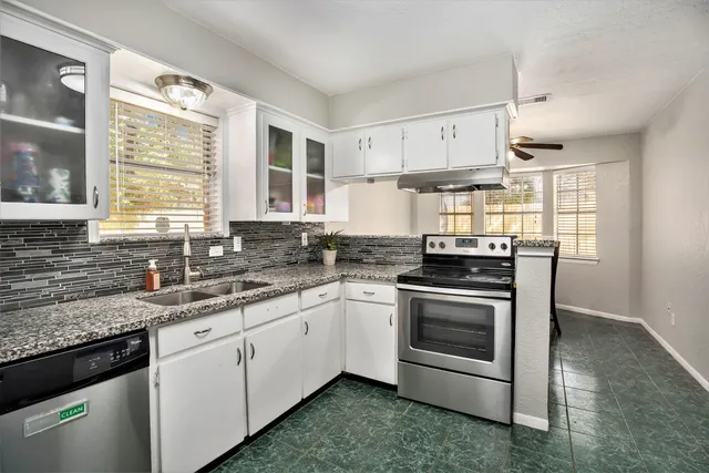 a kitchen with stainless steel appliances granite countertop a sink a stove a refrigerator and white cabinets
