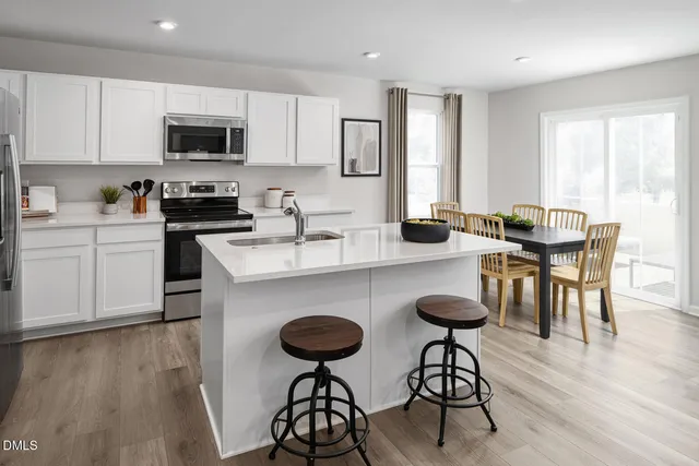 a kitchen with stainless steel appliances granite countertop a stove a sink a microwave a dining table and chairs with wooden floor