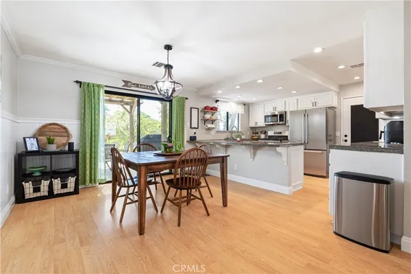a kitchen with stainless steel appliances granite countertop a stove a refrigerator a kitchen island a dining table and chairs with wooden floor