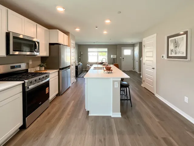 a kitchen with stainless steel appliances a stove a sink dishwasher a refrigerator white cabinets and wooden floor