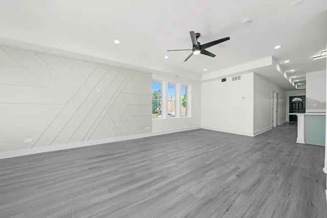 a view of an empty room with wooden floor and a ceiling fan