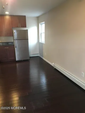 a view of a refrigerator in kitchen and an empty room with wooden floor