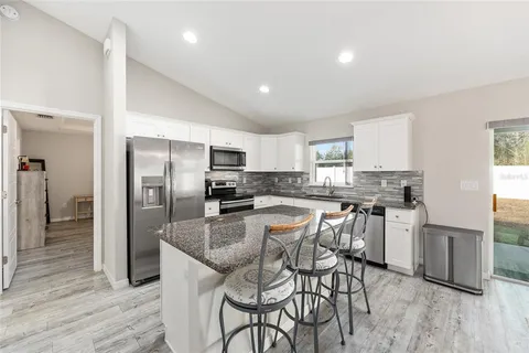 a kitchen with stainless steel appliances kitchen island granite countertop a refrigerator a stove a sink a dining table and chairs