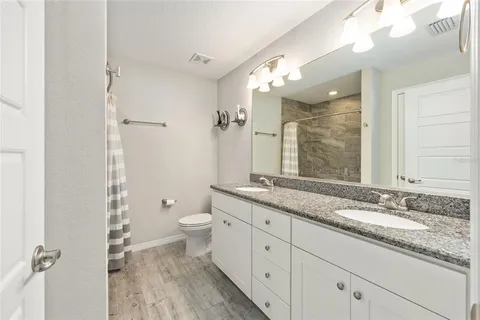 a bathroom with a granite countertop double vanity sink a mirror and a toilet