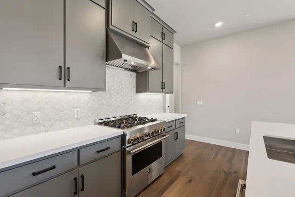 a kitchen with stainless steel appliances a stove and white cabinets with wooden floor