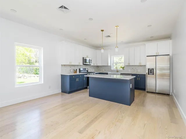a kitchen with stainless steel appliances kitchen island granite countertop a stove a refrigerator a sink dishwasher and white cabinets with wooden floor