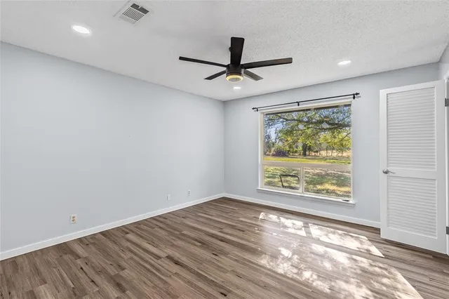 an empty room with wooden floor ceiling fan and windows