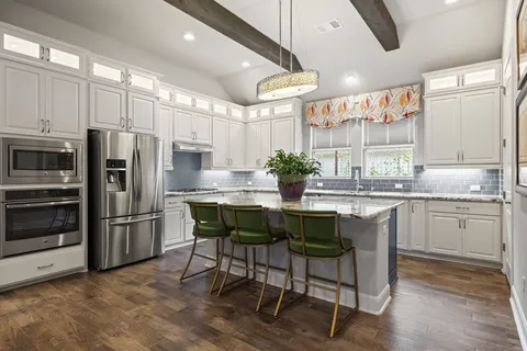 a kitchen with granite countertop a table chairs microwave and refrigerator