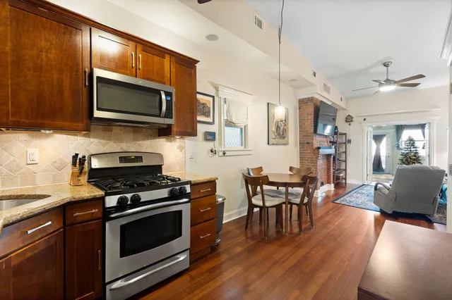 a kitchen with stainless steel appliances a stove a sink a microwave a dining table and chairs with wooden floor