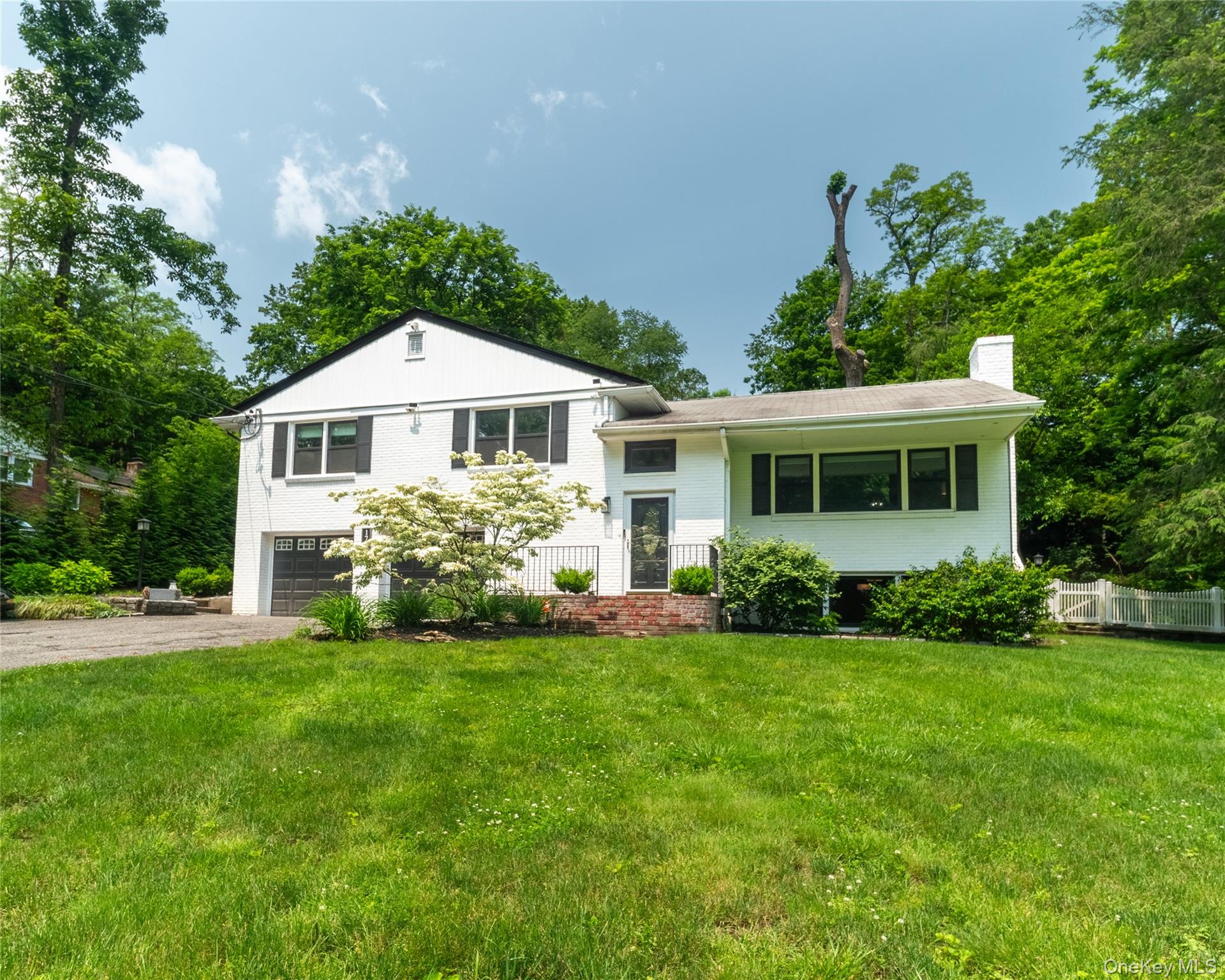 Tri-level home with driveway, a chimney, brick siding, and an attached garage