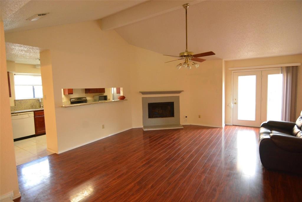 210 Apollo Road Garland, TX 75040 - Photo 7 of 23 Spacious room featuring vaulted ceilings, wood-finish flooring, a fireplace with a stone surround, and double glass panel doors