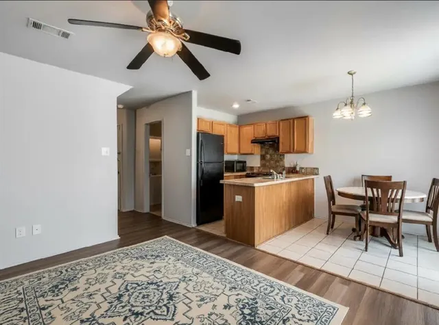 a kitchen with stainless steel appliances kitchen island granite countertop a refrigerator a stove a sink a dining table and chairs with wooden floor