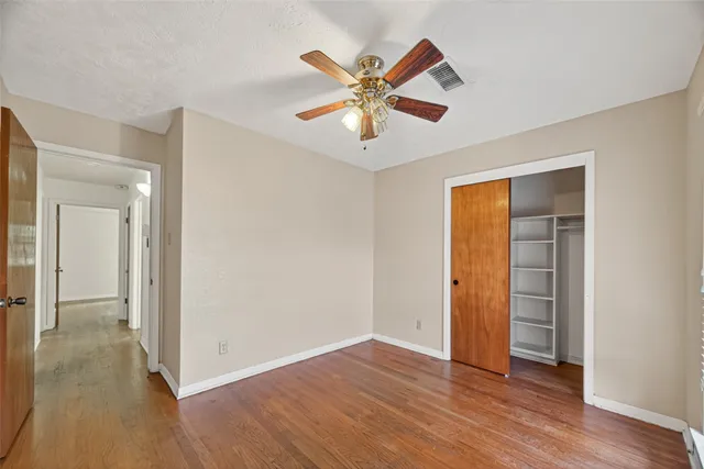 a view of an empty room with wooden floor and a ceiling fan