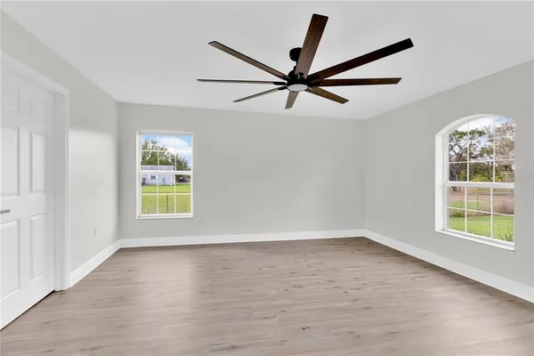 an empty room with wooden floor ceiling fan and windows