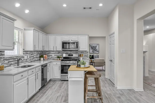 a kitchen with stainless steel appliances a stove a sink dishwasher a refrigerator and white cabinets with wooden floor