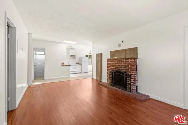 a view of an empty room with wooden floor fireplace and a window