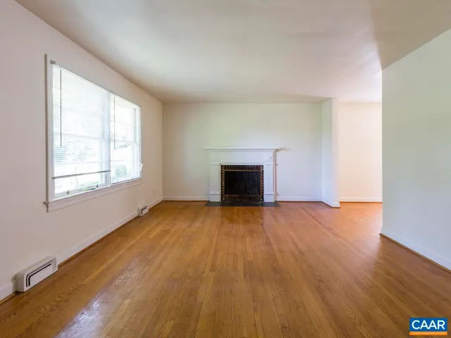 an empty room with wooden floor a fireplace and windows