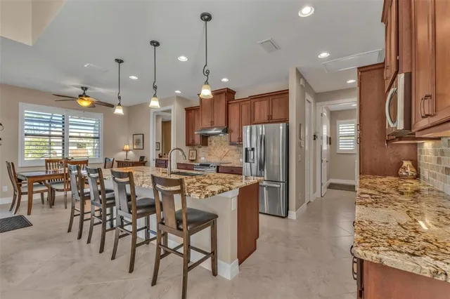 a kitchen with stainless steel appliances granite countertop a stove top oven a refrigerator a sink and chairs