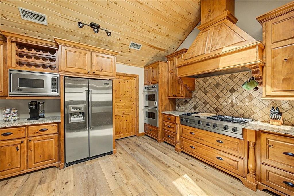 Vaulted wood-paneled ceiling, stainless steel appliances, wood-finish flooring, custom wood cabinetry, and tile backsplash