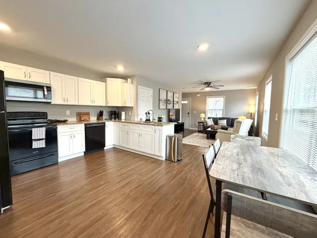 a living room with stainless steel appliances granite countertop furniture wooden floor and a kitchen view