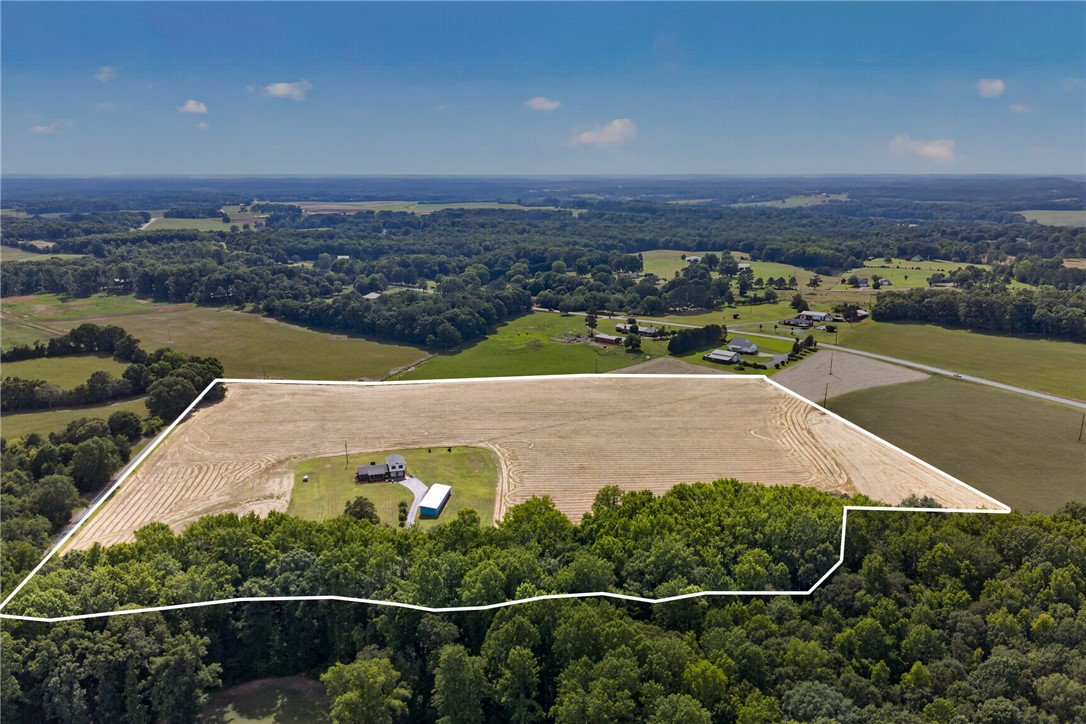145 State Rd S-4-935 Pendleton, SC 29670 - Photo 2 of 47 A sprawling rural landscape featuring a house with outbuildings amidst fields and lush tree lines.