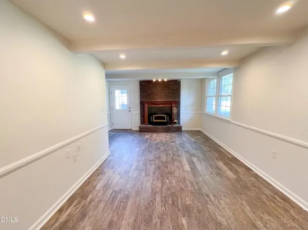 an empty room with wooden floor fireplace and windows