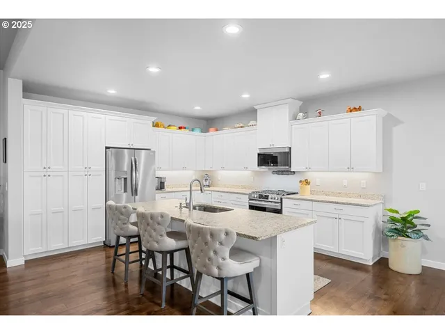 a kitchen with stainless steel appliances kitchen island granite countertop a dining table chairs and white cabinets