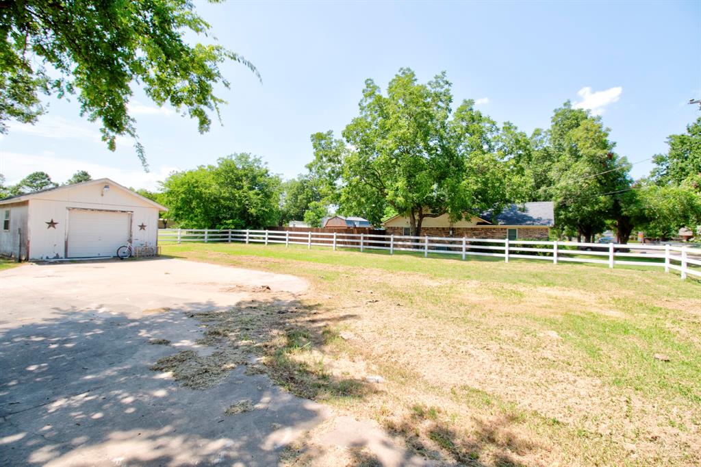 503 Sherman Street Tioga, TX 76271 - Photo 8 of 13 Detached garage structure with a roll-up door, paved driveway, expansive lawn area, white ranch fencing, and mature trees