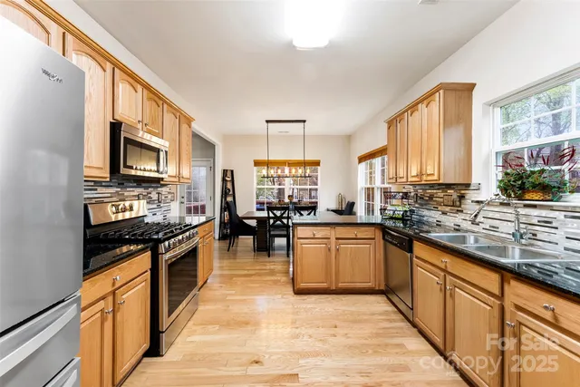 a kitchen with stainless steel appliances granite countertop a stove top oven a sink dishwasher a dining table and chairs with wooden floor