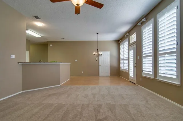 an empty room with chandelier fan and windows