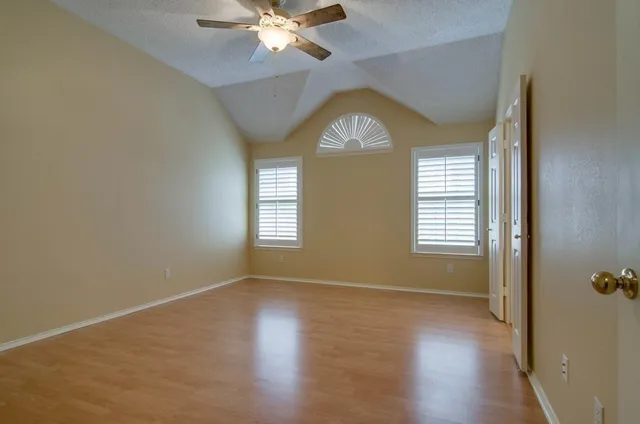 an empty room with wooden floor fan and windows