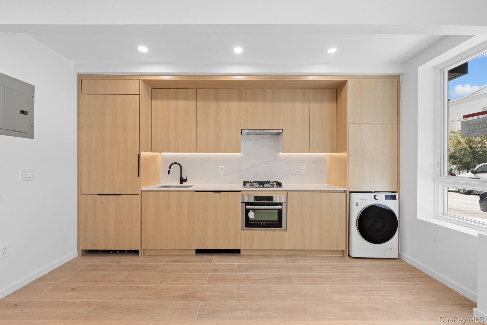 366 Harman Street, Unit 1F Brooklyn, NY 11237 - Photo 4 of 12 Kitchen with light brown cabinetry, modern cabinets, washer / clothes dryer, appliances with stainless steel finishes, and light stone countertops