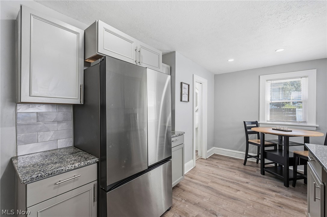 3386 Sylvanhurst Road Cleveland Heights, OH 44112 - Photo 12 of 46 Kitchen space featuring light gray cabinetry, granite countertops, a stainless steel refrigerator, a gray tile backsplash, and wood-finish flooring