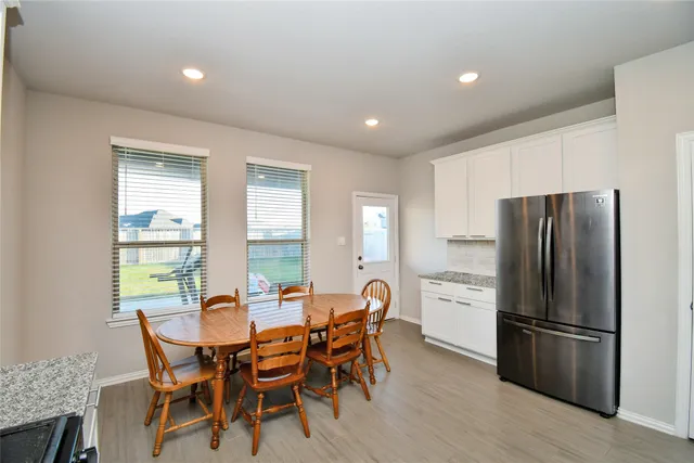 a kitchen with stainless steel appliances a dining table chairs refrigerator and wooden floor