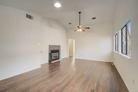 a view of an empty room with wooden floor kitchen view and a window